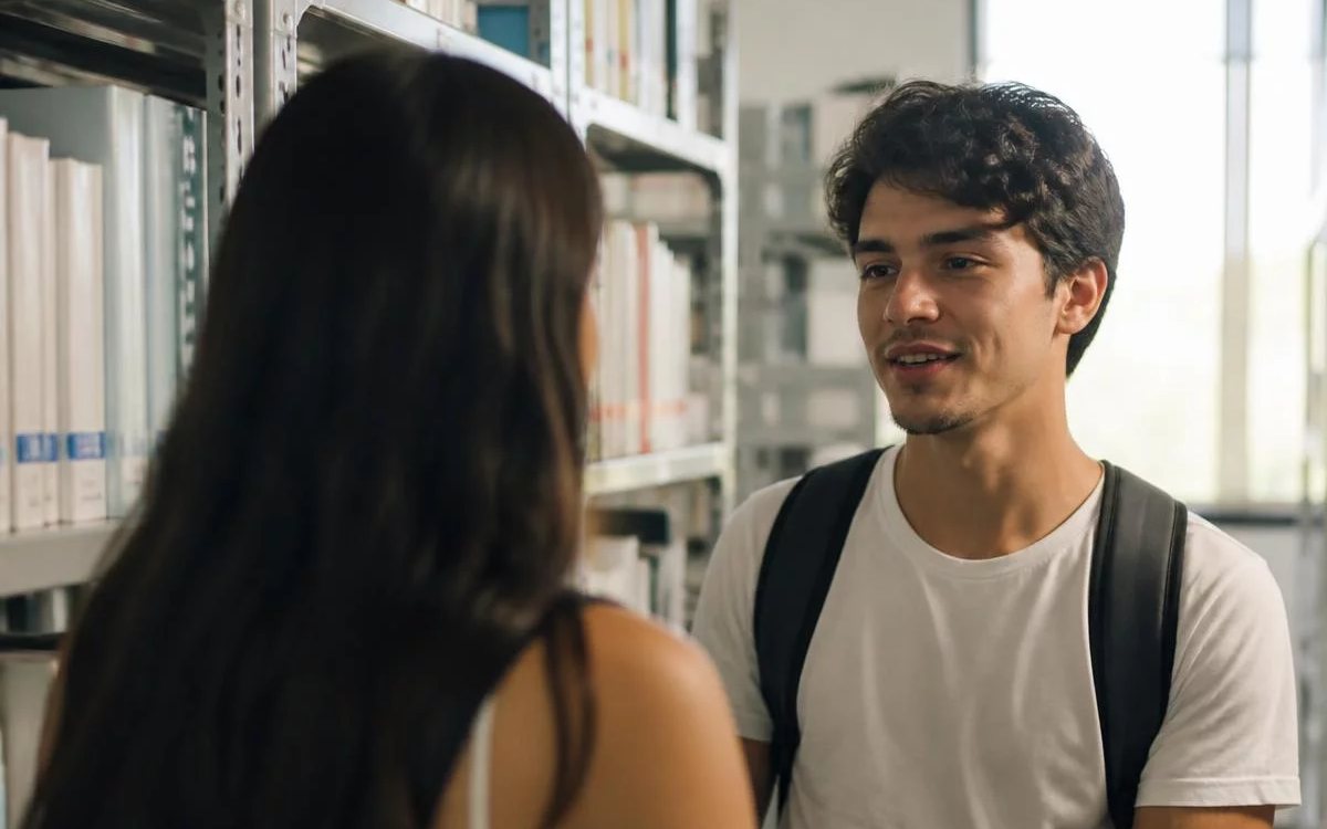 Três pessoas sentadas a uma mesa comprida, no meio de uma conversa numa sala de janelas altas